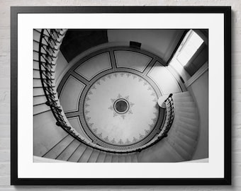 May include: A black and white photograph of a spiral staircase in a building with a patterned ceiling. The staircase is made of stone and has a wrought iron railing. The ceiling is decorated with a circular pattern.