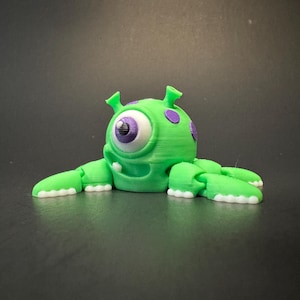 May include: A green, 3D printed, one-eyed monster with purple spots and white teeth. The monster has six legs and is lying on its belly.