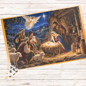 Op de afbeelding: Een rechthoekige legpuzzel met een kersttafereel met een centrale kribbe, figuren in gewaden, schapen en een engel aan de nachtelijke hemel. De puzzelstukjes liggen verspreid in de linkerbenedenhoek en tonen een gedetailleerde illustratie van een stal.
