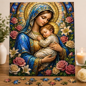 Peut inclure: Un puzzle représentant une illustration de style vitrail d'une femme portant un voile bleu et tenant un enfant. La scène est encadrée de roses et de lys roses et blancs, avec un halo doré derrière eux. Des pièces de puzzle sont éparpillées.