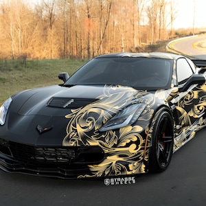 Könnte beinhalten: Schwarzes Sportwagen mit goldenem floralem Design. Das Auto hat ein schlankes, aerodynamisches Design mit schwarzen Rädern und einem Spoiler. Das Auto steht auf einer asphaltierten Straße mit Bäumen im Hintergrund. Der Text "STRASSE WHEELS" ist sichtbar.
