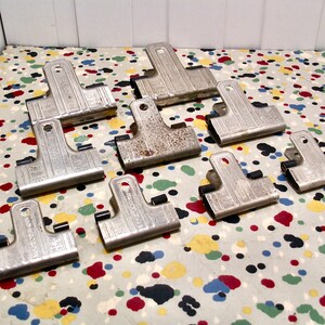 May include: A collection of eight silver binder clips with black rubber grips. The clips are arranged on a white surface with colorful polka dots.