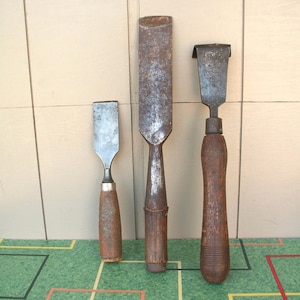 May include: Three vintage wood chisels with metal blades and wooden handles. The chisels vary in size and shape, showing signs of wear and use. The handles are a dark brown color.