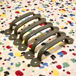 May include: Set of six green metal drawer pulls. The pulls are shaped like a half-circle with a rounded edge. They are arranged in a row, with the largest pull at the top and the smallest pull at the bottom.