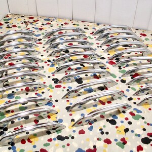 May include: A collection of 20 silver-toned cabinet door pulls with a mid-century modern design. The pulls are arranged in rows on a white surface with colorful polka dots.