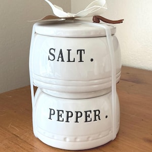 Könnte beinhalten: Eine weiße Keramik-Tasse mit schwarzem Henkel und dem Text "But First, Coffee" in fetter, schwarzer Schrift. Die Tasse steht vor einem verschwommenen Hintergrund. Die Tasse ist etwa 10 cm hoch.