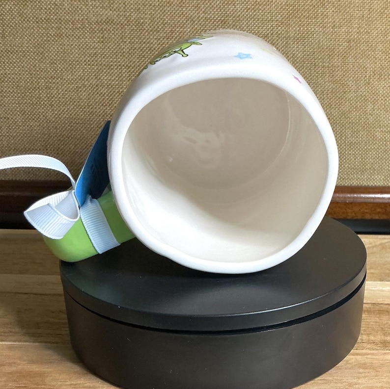 May include: A white ceramic mug with a black handle and the text "But First, Coffee" in a bold, black font. The mug is set against a blurred background, highlighting its clean design.