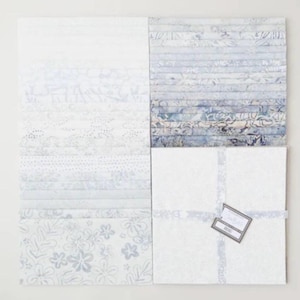 May include: A collection of fabric squares in shades of white and blue, arranged in a grid. The fabrics feature various patterns, including floral, dotted, and striped designs. A tag is attached to a bundle of white squares.