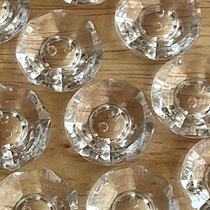 May include: Close-up of several clear, faceted glass cabinet knobs with a central, circular, brass-colored insert. The knobs are arranged on a light brown wooden surface, showcasing their reflective qualities.