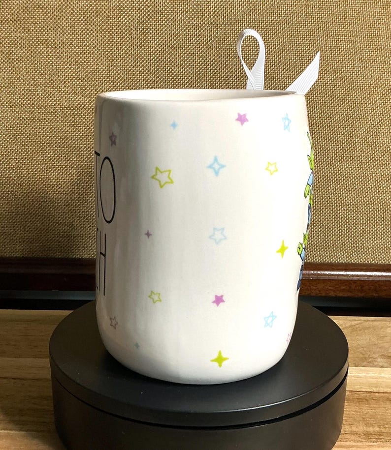 May include: A white ceramic mug with a black handle and the text "But First, Coffee" in a black, handwritten-style font. The mug is on a white surface.