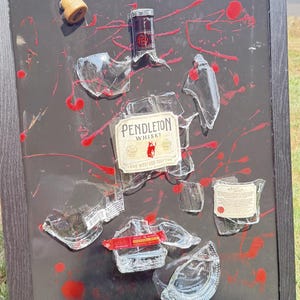 May include: A framed artwork featuring shattered glass pieces and a whiskey bottle label. The black background has red paint splatters. The label reads "Pendleton Whisky True Western Tradition."
