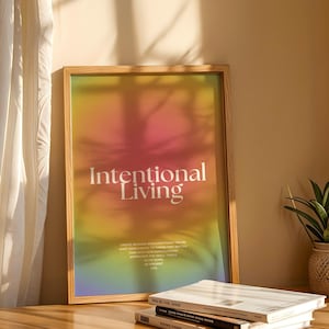 Może przedstawiać: Oprawiony wydruk z napisem "Intentional Living" w kolorze białym na kolorowym tle gradientowym w kolorze różowym, żółtym i pomarańczowym. Wydruk znajduje się w jasnej drewnianej ramie i spoczywa na drewnianej powierzchni z książkami i małą rośliną doniczkową.