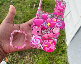 Könnte beinhalten: Ein pinkfarbenes, mit Schmucksteinen besetztes Handycase und ein passendes Armband. Das Handycase ist mit pinkfarbenen Herzen, einer Kamera, einem Lolli und dem Wort "Sweet" verziert. Das Armband ist ebenfalls pink und mit kleinen pinkfarbenen Schmucksteinen verziert.