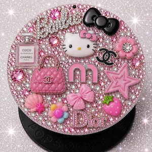 May include: A bedazzled pink PopSockets grip featuring various charms, including a Hello Kitty face, a black bow, a pink handbag, and the Dior logo. The surface is covered in pink rhinestones and other decorative elements.