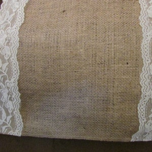 May include: A burlap table runner with white lace trim. The lace has a floral pattern.