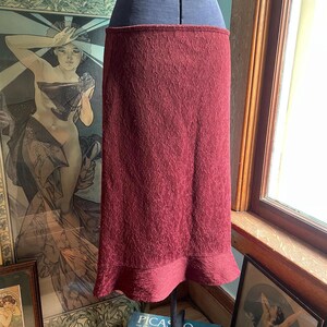 May include: A burgundy skirt with a textured fabric and a ruffled hem.