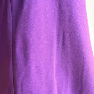 May include: Close-up of a vibrant purple fabric. The material has a subtle texture and a smooth appearance. The color is a rich, saturated shade of purple, with slight variations in tone across the surface. The fabric appears to be a solid color.