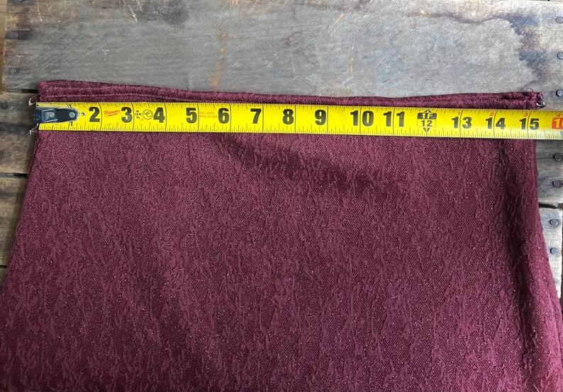 May include: A burgundy fabric with a textured pattern. The fabric is measured with a tape measure, showing a length of 15 inches.