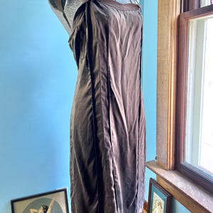 May include: A dark brown sleeveless dress on a mannequin, featuring a straight neckline with a darker brown trim, thin shoulder straps, and vertical seam detailing running down the front of the garment, creating a structured and simple silhouette.