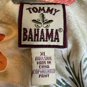 May include: Close-up of a Tommy Bahama shirt tag. The tag is rectangular with a maroon border and the brand name in maroon. The tag reads "XL 100% Silk Made in China Copyrighted Print."