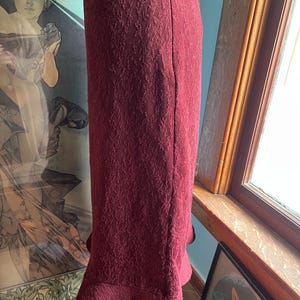 May include: A burgundy skirt with a textured pattern and a ruffled hem. The skirt has a back zipper closure.