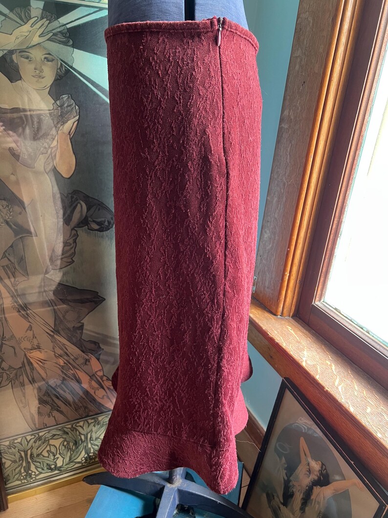 May include: A burgundy skirt with a textured pattern and a ruffled hem. The skirt has a back zipper closure.