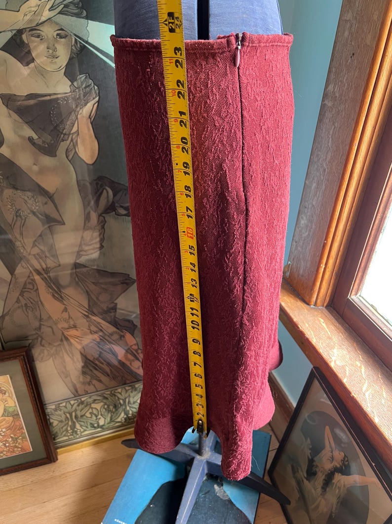 May include: A burgundy skirt with a textured pattern and a zipper closure. The skirt is approximately 23 inches long.