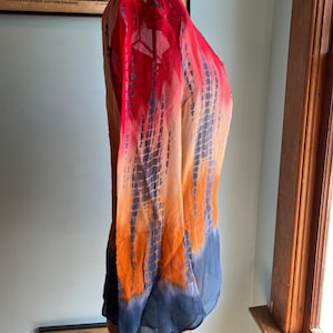 Peut inclure: Un chemisier &agrave; manches longues tie-dye aux tons de rouge, orange et bleu. Le tissu transparent est drap&eacute; sur un mannequin, mettant en valeur le d&eacute;grad&eacute; de couleurs. Une affiche de la compagnie ferroviaire Rio Grande est visible.