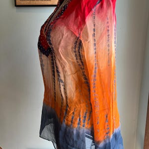 Peut inclure: Une tunique transparente &agrave; manches longues dans un d&eacute;grad&eacute; de couleurs vives. Le haut passe du rouge aux &eacute;paules &agrave; l'orange puis au bleu &agrave; l'ourlet. Le tissu a un effet tie-dye avec des stries bleues verticales.