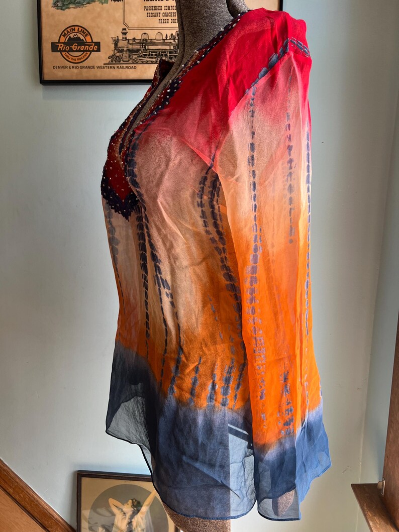 Peut inclure: Une tunique transparente &agrave; manches longues dans un d&eacute;grad&eacute; de couleurs vives. Le haut passe du rouge aux &eacute;paules &agrave; l'orange puis au bleu &agrave; l'ourlet. Le tissu a un effet tie-dye avec des stries bleues verticales.