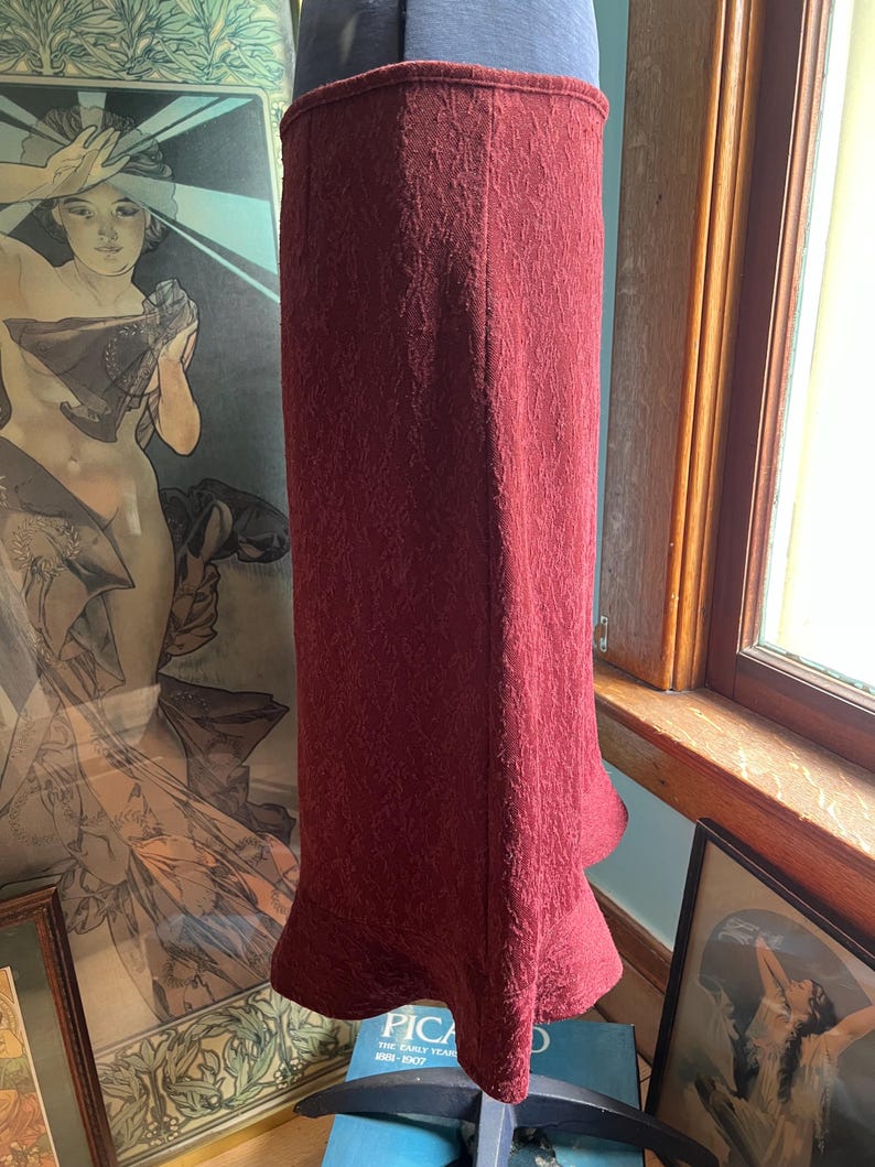May include: A burgundy midi skirt with a textured pattern and a flared hem.