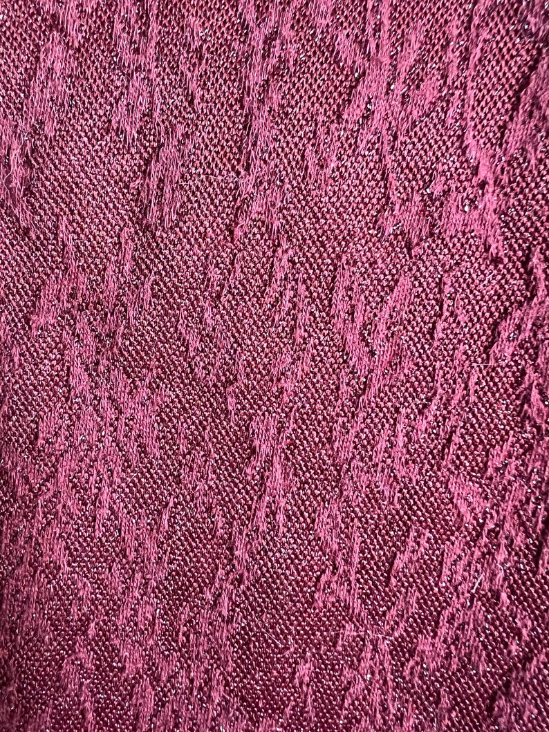 May include: Close-up of a deep burgundy fabric with a textured, woven pattern. The fabric has a subtle shimmer.
