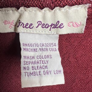 May include: A white care label with the text "free People" in purple lettering, followed by the text "RN66170 CA32054 MACHINE WASH COLD WASH COLORS SEPARATELY NO BLEACH TUMBLE DRY LOW".