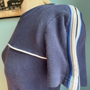 K&ouml;nnte beinhalten: Marineblaues Kurzarm-T-Shirt mit wei&szlig;er Paspelierung und gestreiften Akzenten am &Auml;rmel. Die Streifen umfassen Blau- und Wei&szlig;t&ouml;ne. Das Shirt wird auf einer Schaufensterpuppe pr&auml;sentiert.