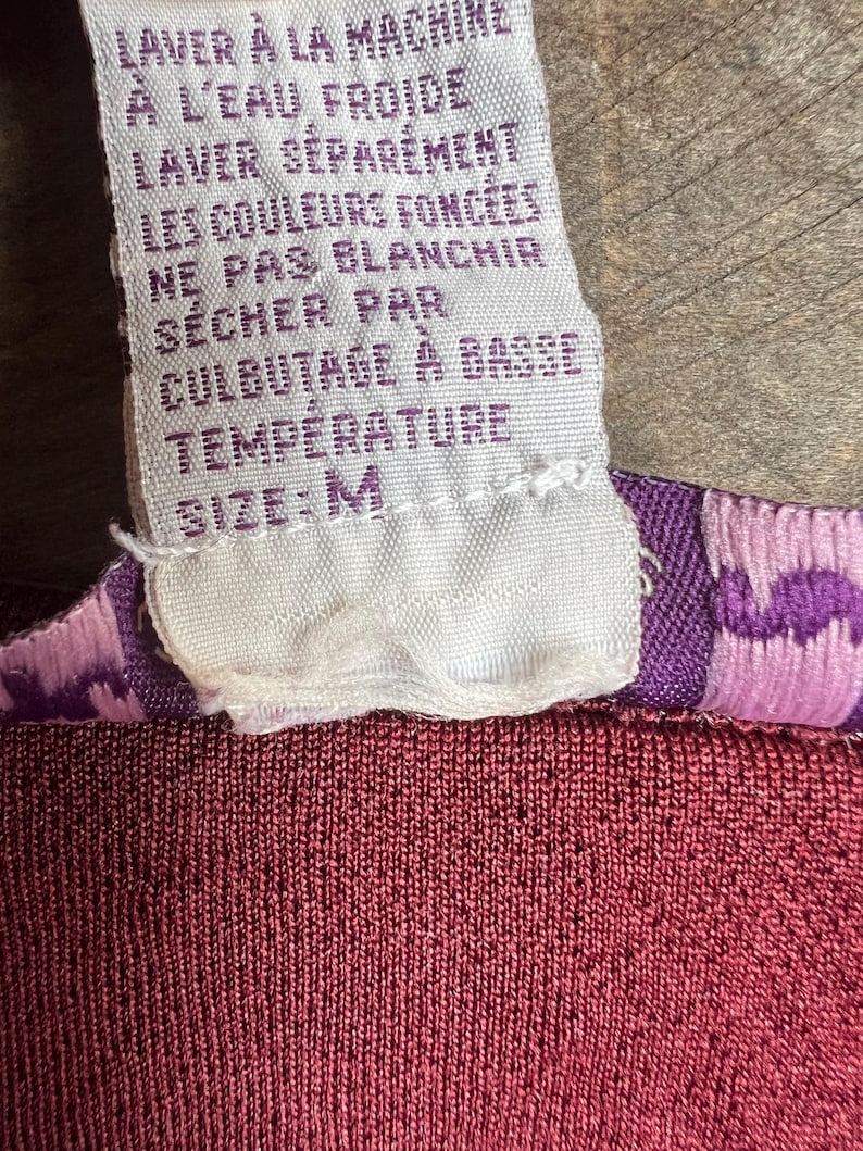 May include: White care label with instructions for washing and drying a garment in French. The label reads "LAVER &Agrave; LA MACHINE &Agrave; L'EAU FROIDE LAVER S&Eacute;PAR&Eacute;MENT LES COULEURS FONC&Eacute;ES NE PAS BLANCHIR S&Eacute;CHER PAR CULBUTAGE &Agrave; BASSE TEMP&Eacute;RATURE SIZE: M".