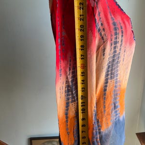 Peut inclure: V&ecirc;tement color&eacute; de style tie-dye, rouge, orange et bleu. Le tissu est drap&eacute; sur un mannequin, avec un m&egrave;tre ruban indiquant une longueur d'environ 63,5 cm. Le v&ecirc;tement a un aspect fluide et l&eacute;ger.