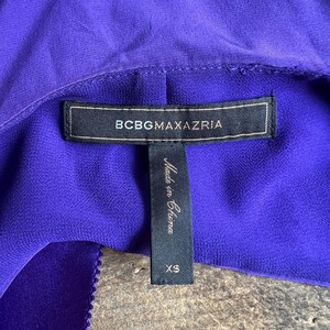 May include: Close-up of a vibrant purple garment with a label that reads "BCBGMAXAZRIA." A smaller tag below indicates the garment is size XS and "Made in China."