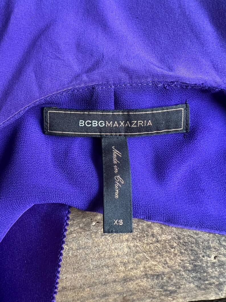 May include: Close-up of a vibrant purple garment with a label that reads "BCBGMAXAZRIA." A smaller tag below indicates the garment is size XS and "Made in China."
