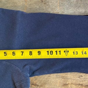 K&ouml;nnte beinhalten: Ein marineblaues Langarmshirt mit hellblau-wei&szlig;em Streifen am &Auml;rmel. Das Shirt wird mit einem gelben Ma&szlig;band gemessen und hat eine L&auml;nge von ca. 40 cm.