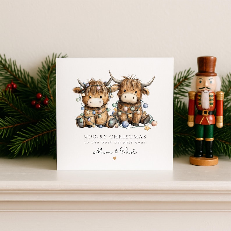 May include: A square white greeting card featuring an illustration of two brown Highland cows tangled in colorful Christmas lights. The text reads MOO-RY CHRISTMAS TO THE BEST PARENTS EVER Mum & Dad with a small gold heart symbol below the text.
