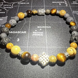 May include: A beaded bracelet with a silver Buddha charm and a silver knot charm. The bracelet features brown, black, and gold beads.