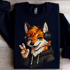 May include: Dark navy blue sweatshirt with a cartoon fox illustration. The fox has orange fur, blue eyes, and black headphones. It's wearing a black hoodie and giving a peace sign. The design is printed on the front of the sweatshirt.