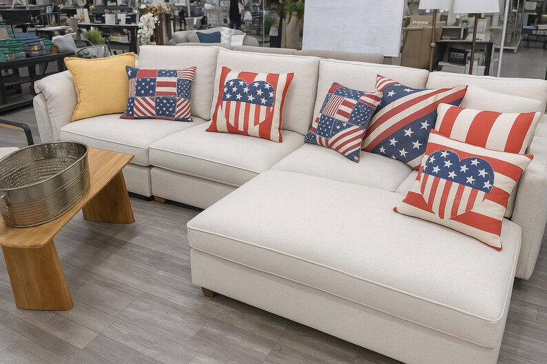 May include: A white corner sofa with cushions featuring American flag patterns in red, white, and blue. A wooden side table with a metal tub is in the foreground. The sofa is a prominent piece of furniture.