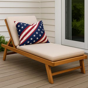 May include: A wooden sun lounger with a beige cushion and a decorative pillow. The pillow has a patriotic design with red and white stripes and blue with white stars. The lounger is on a wooden deck.