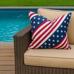 May include: A cushion with a design inspired by the American flag. The cushion has a blue field with white stars and red and white stripes. It sits on a beige outdoor sofa with a wicker frame, near a swimming pool.