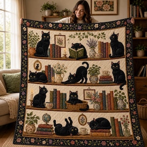 May include: A quilted throw blanket featuring a repeating pattern of black cats, stacks of colorful books, potted plants, and floral framed art. The border is dark with a floral motif, and the background is a cream-colored quilted fabric.