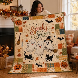 May include: A quilted throw blanket featuring a patchwork border of orange, green, and plaid squares. The center displays three white ghosts, two black cats, and the text Spooky Season in brown script, surrounded by pumpkins, bats, and leaves.