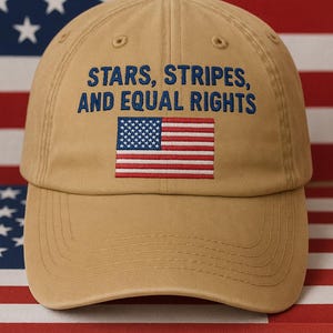 Puede incluir: Gorra de béisbol beige con la inscripción bordada "STARS, STRIPES, AND EQUAL RIGHTS" y una bandera estadounidense. La gorra se muestra sobre un fondo de la bandera estadounidense.