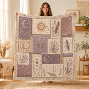 May include: A rectangular woven throw blanket featuring a patchwork design of celestial and botanical motifs in shades of purple, cream, and gold. The pattern includes a sun, moon phases, a butterfly, crystals, feathers, and a hand holding a crystal.