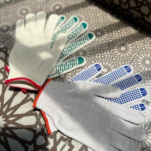 May include: Two pairs of work gloves. One pair is light gray with red trim and blue dotted grips. The other pair is off-white with green grips and red trim. The gloves are made of a knitted material.
